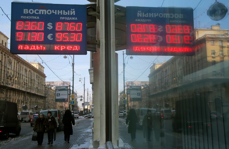 © Reuters. People walk near a board showing currency exchange rates in Moscow