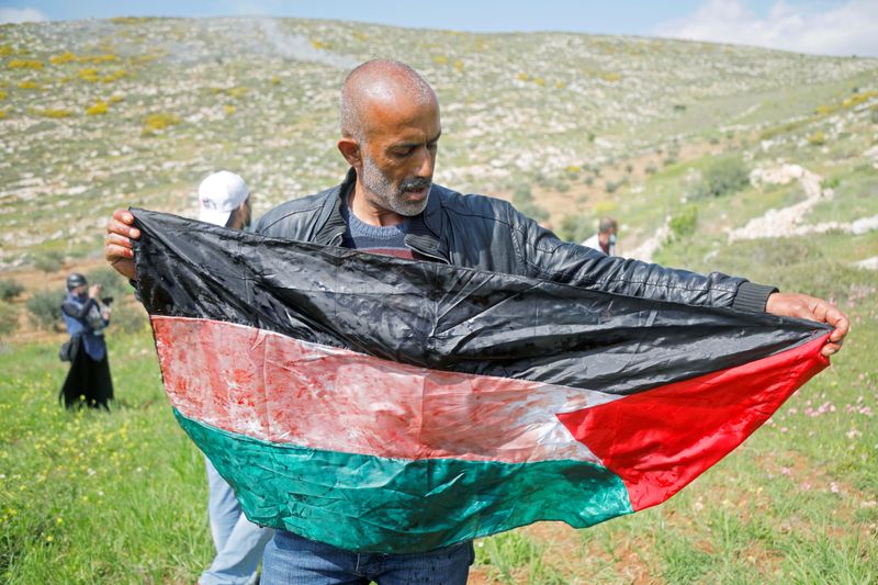 &copy; Reuters. Un hombre sostiene una bandera palestina manchada de sangre de un palestino herido de muerte durante una protesta contra los asentamientos israelíes, en Beit Dajan, en Cisjordania,