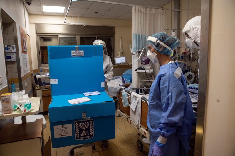 © Reuters. Hospital employees stand next to a mobile voting booth and box as they make their way to assist patients in a ward for the treatment of the coronavirus disease (COVID-19), to vote in Israel's general election, at Sheba Medical Center in Ramat Gan