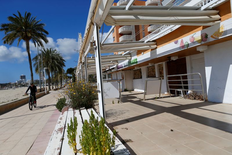 &copy; Reuters. A man rides his bicycle next to closed terrace bars in Magaluf beach