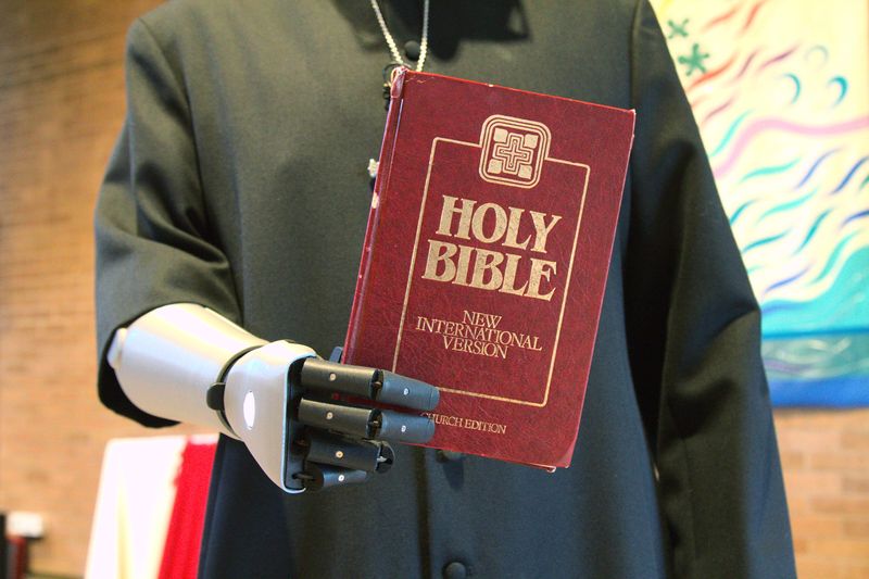 &copy; Reuters. Priest-in-training Daniel Cant holds a bible as he demonstrates his bionic arm by British company Open Bionics at Christ Church in Colchester