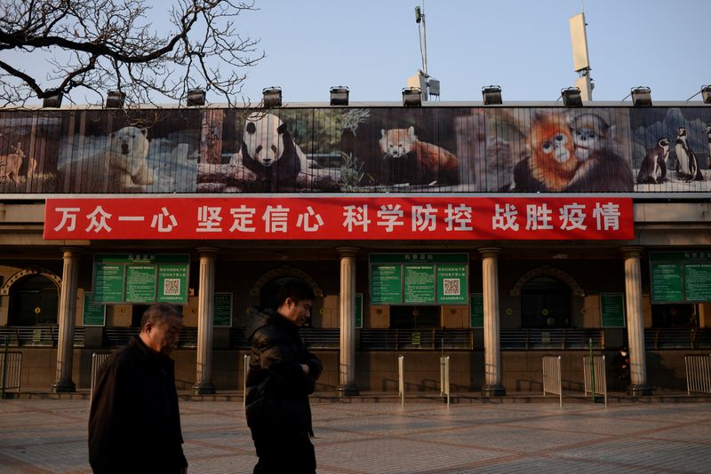 &copy; Reuters. FILE PHOTO: Men walk past a banner hung on the ticket office of the Beijing Zoo that is closed following an outbreak of the novel coronavirus in the country, in Beijing