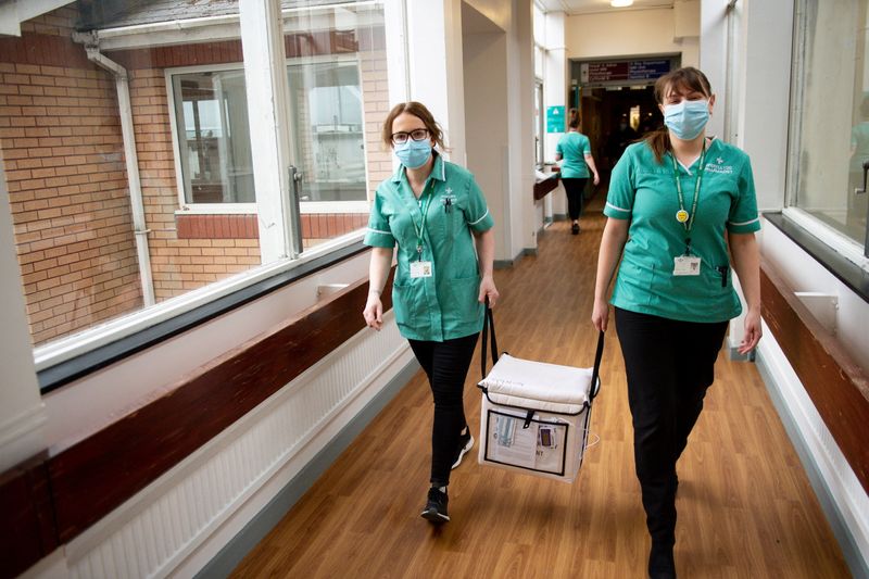 &copy; Reuters. Dos farmacéuticas transportan un refrigerador con vacunas de Moderna contra el coronavirus en el Hospital General Glangwili de Carmarthen, Gales.