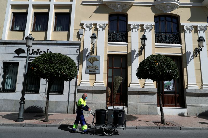 &copy; Reuters. FOTO DE ARCHIVO: Un empleado de limpieza municipal empuja un carrito frente a una sucursal de Unicaja en el centro de Ronda