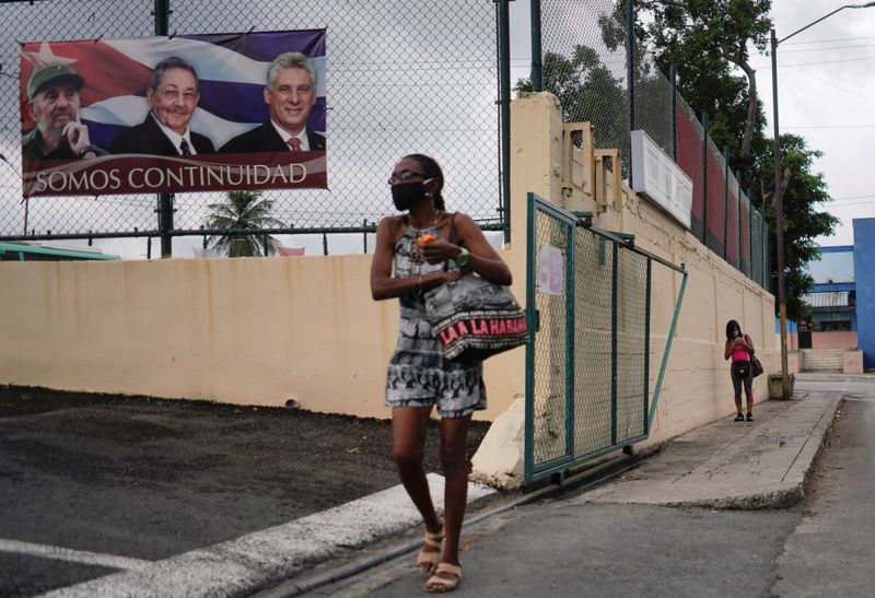 &copy; Reuters. Foto de archivo de una mujer caminando en La Haban cerca de un cartel con las fotos de Fidel Castro, Raul Castro y Miguel Diaz Canel