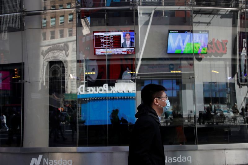 &copy; Reuters. A man with a face mask walks by television screens outside the Nasdaq Market Site, after further cases of coronavirus were confirmed in New York, at Times Square in New York