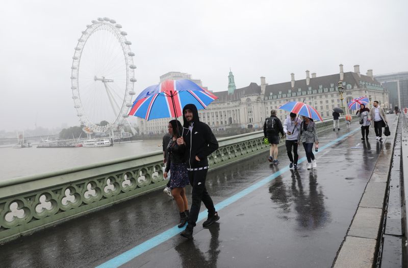 &copy; Reuters. People holding Union Jack themed umbrellas take a stroll in the rain  at Westminster Bridge near the London Eye in London