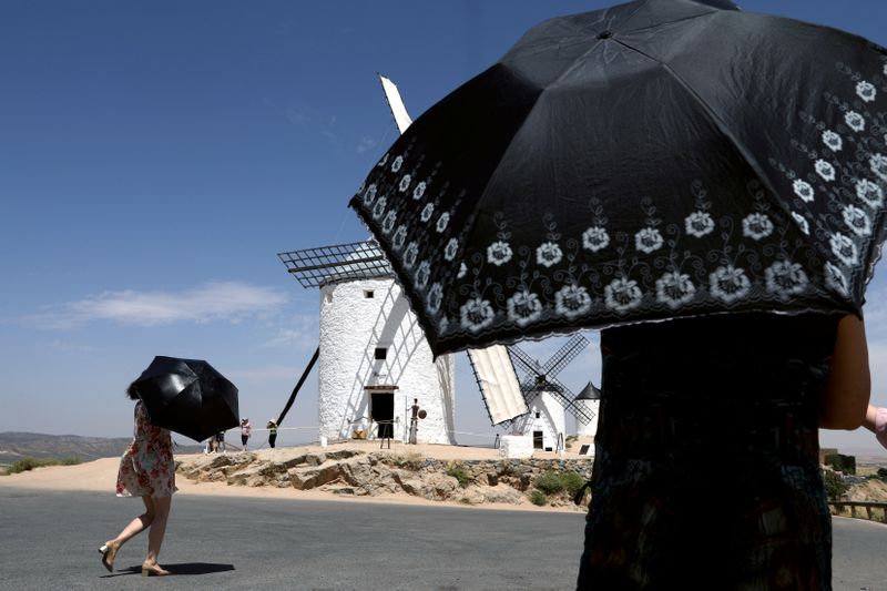 &copy; Reuters. Turistas se protegen del calor bajo paraguas mientras visitan los molinos de viento de La Mancha durante una ola de calor en Consuegra