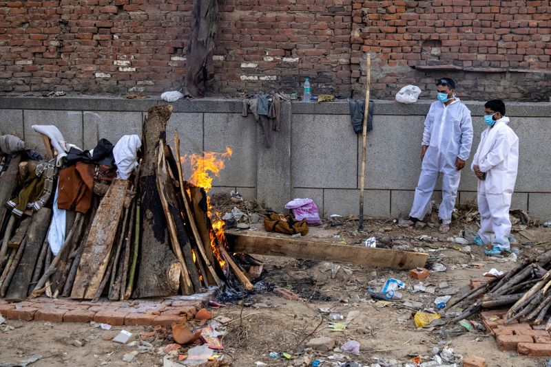 &copy; Reuters. Relatives stand next to the burning funeral pyre of a person, who died due to the coronavirus disease (COVID-19), at a crematorium ground in New Delhi