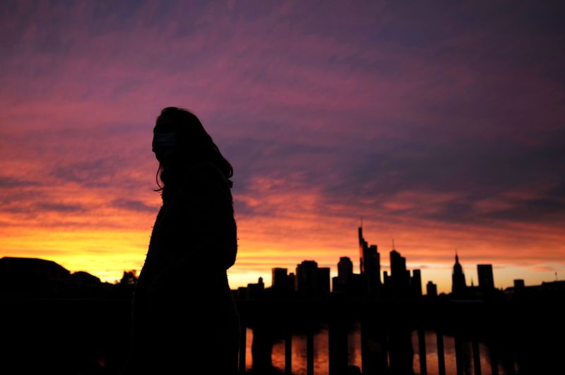 &copy; Reuters. FILE PHOTO: A woman wearing a protective mask walks past the skyline of the financial district during sunset as the spread of the coronavirus disease (COVID-19) continues in Frankfurt