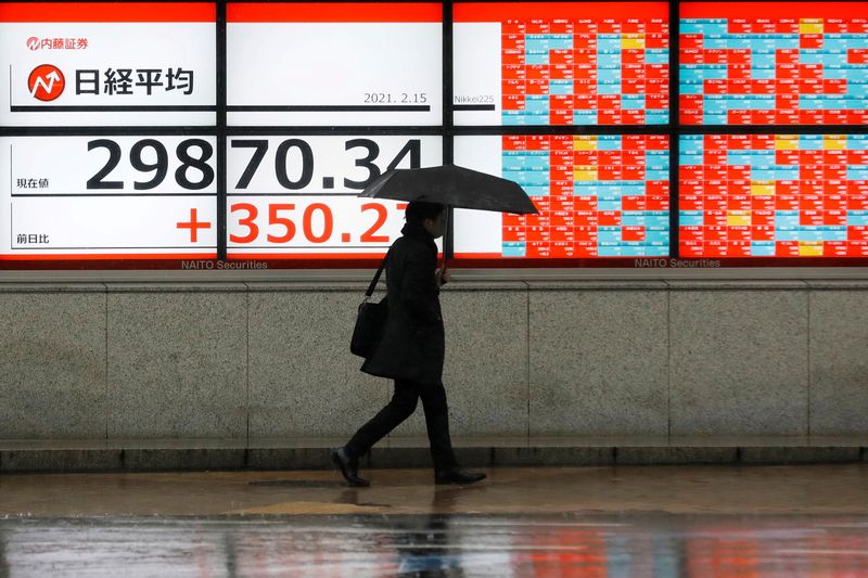 &copy; Reuters. A man holding an umbrella walks in front of an electric board showing Nikkei index a brokerage in Tokyo