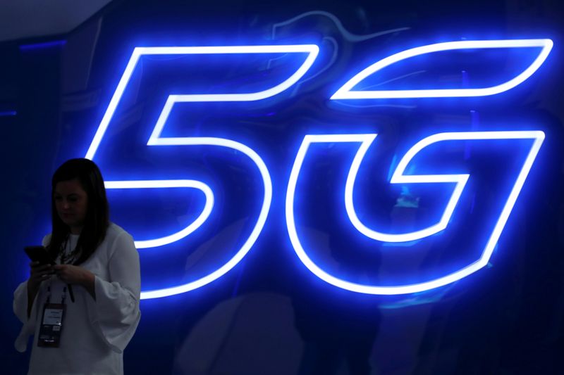 © Reuters. FOTO DE ARCHIVO: Una mujer mira su teléfono móvil junto a un cartel de 5G en el Mobile World Congress en Barcelona, España