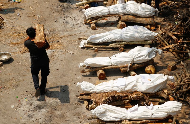 &copy; Reuters. A man carrying wood walks past the funeral pyres at a crematorium in New Delhi