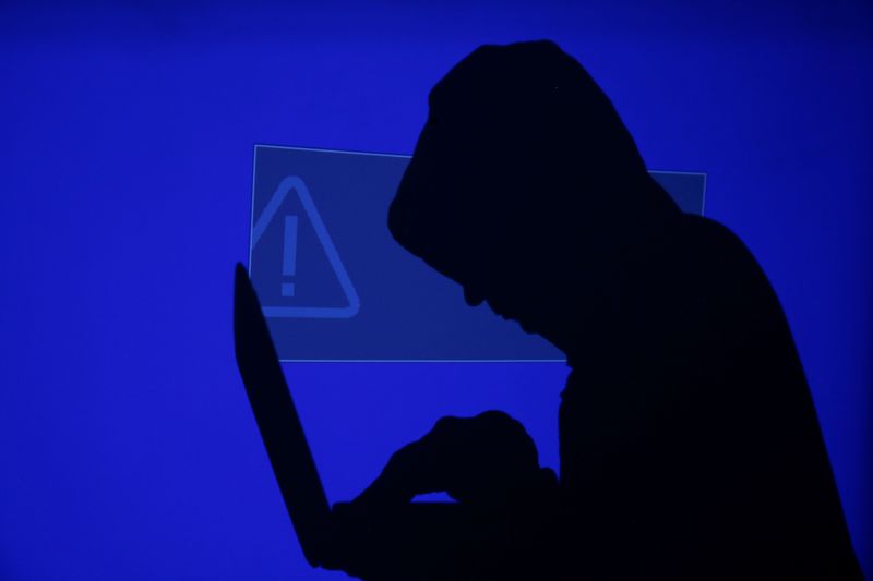 &copy; Reuters. IMAGEN DE ARCHIVO. Un hombre encapuchado sostiene una computadora portátil mientras se proyecta una pantalla azul con un signo de exclamación en esta ilustración