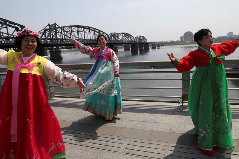 &copy; Reuters. FILE PHOTO: Tourists dressed in North Korean costumes dance as they pose for pictures near the Friendship Bridge and Broken Bridge over the Yalu River, which separates North Korea's Sinuiju from China, in Dandong, Liaoning province, China April 21, 2021. 