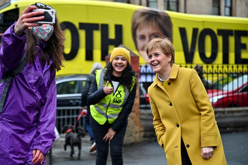 © Reuters. Scotland's First Minister Nicola Sturgeon and candidate Roza Salih pose for a selfie with a voter at Annette Street School polling station as the Scottish parliamentary election voting has begun, in Glasgow, Britain, May 6, 2021 . Jeff J Mitchell/Pool via REUTERS