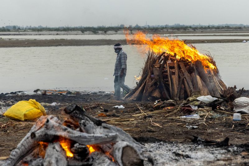 © Reuters. A man walks past burning pyres with people who died from the coronavirus disease (COVID-19), on the banks of the river Ganges at Garhmukteshwar in the northern state of Uttar Pradesh, India, May 6, 2021. REUTERS/Danish Siddiqui