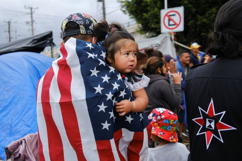 &copy; Reuters. Honduran migrant Kevin, wearing a U.S. flag, holds his daughter Keiry, during a multicultural activity at a makeshift camp at the El Chaparral border port of entry with the U.S., in Tijuana, Mexico April 22, 2021.  REUTERS/Toya Sarno Jordan