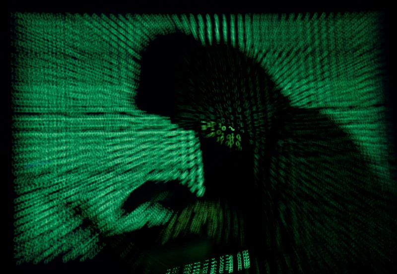 © Reuters. FILE PHOTO: Hooded an holds laptop computer as cyber code is projected on him in this illustration picture
