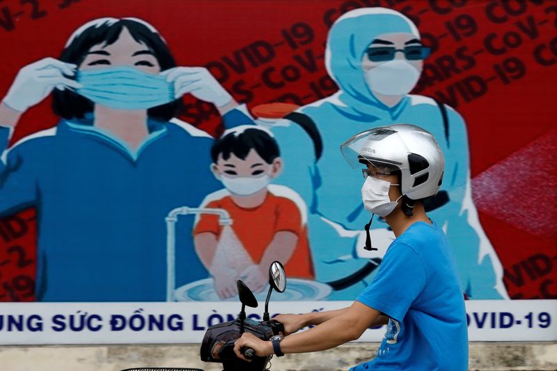 &copy; Reuters. FOTO DE ARCHIVO: Un hombre con mascarilla pasa en motocicleta frente a un cartel para el fomento de la prevención contra la COVID-19 en Hanói, Vietnam, el 31 de julio de 2020. REUTERS/Kham