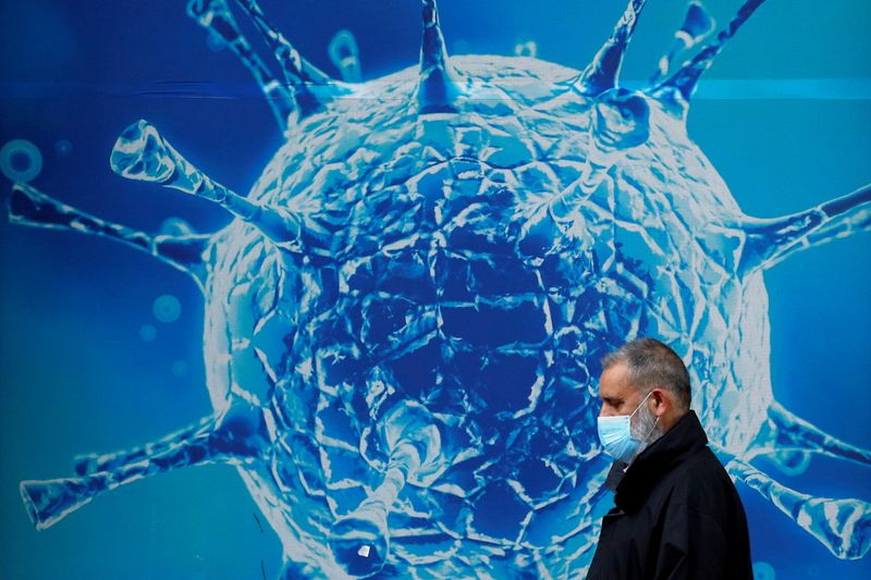 &copy; Reuters. Un uomo con indosso la mascherina passa accanto a una gigantografia di un virus al microscopio. a Oldham, Gran Bretagna, 3 agosto 2020 REUTERS/Phil Noble