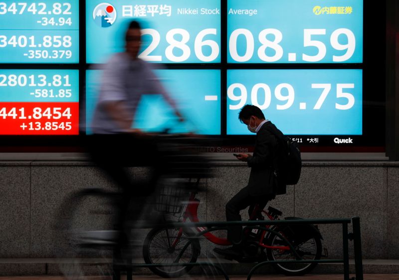 &copy; Reuters. Pessoas de bicicleta passam em frente a painel eletrônico com cotações do mercado financeiro. 11/5/2021. REUTERS/Issei Kato