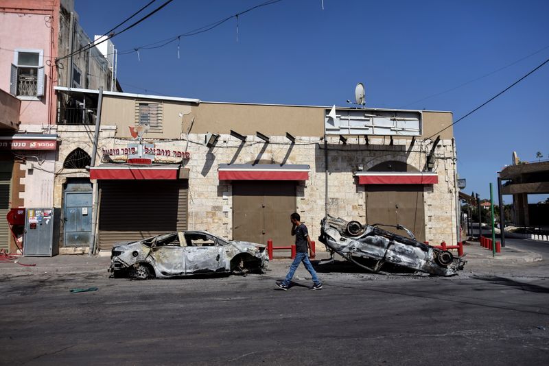 © Reuters. رجل يسير بجوار سيارات محترقة يوم الأربعاء بعد أعمال شغب في بلدة اللد الإسرائيلية. رويترز