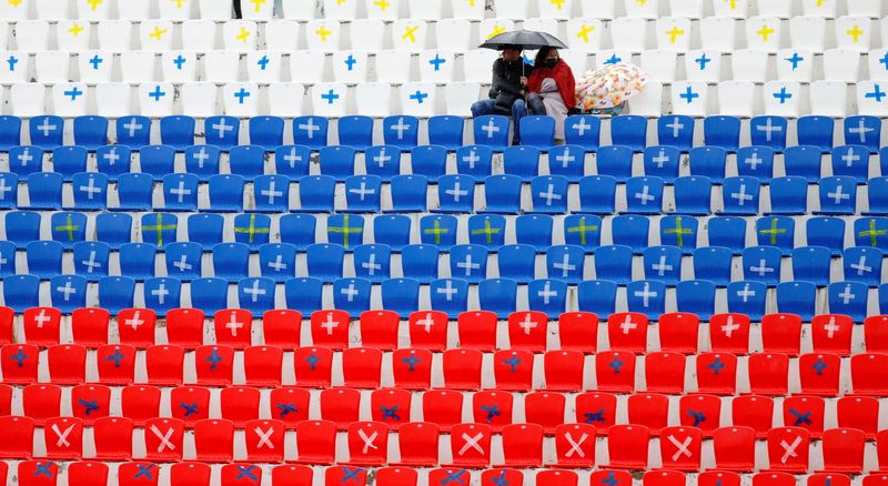 &copy; Reuters. A couple sit under an umbrella amidst empty stadium seats, which depict the colours of the Russian state flag and display signs requesting to keep a social distance amid the coronavirus disease (COVID 19) outbreak, during a football match in Stavropol, Ru