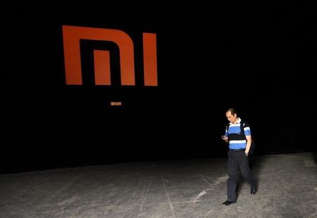 © Reuters. A man checks his mobile phone as he walks past a logo of Xiaomi in Beijing