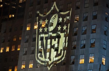 © Reuters. A man stands at a window lit by the NFL logo in New York