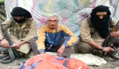 © Reuters. A man who identified himself as Herve Gourdel speaks as he sits in between two masked armed gunmen in this still image taken from video