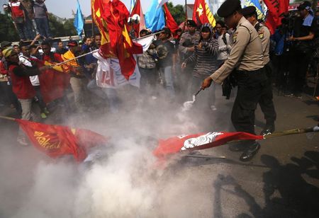 © Reuters. Police use a fire extinguisher to put out burning tyres during a protest by students and activists who are against a bill that would end direct elections for governors and mayors, outside parliament in Jakarta