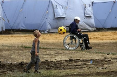 © Reuters. Мальчик и мужчина в инвалидной коляске в лагере беженцев в Ростовской области