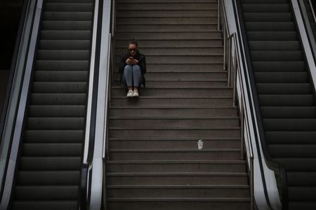 © Reuters. A woman uses her mobile phone as she sits on the stairs at Principe Pio station in Madrid