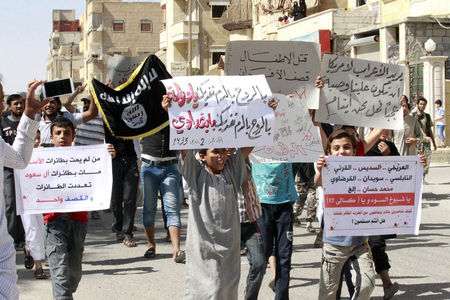 © Reuters. Youths carry banners during a protest against the U.S. airstrikes on the Islamic State (IS) in Raqqa