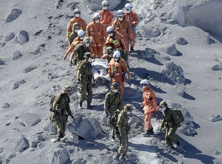 © Reuters. JSDF soldiers and firefighters carry an injured person near a crater of Mt. Ontake, which straddles Nagano and Gifu prefecture