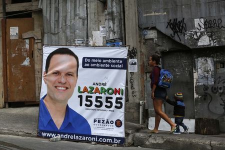 © Reuters. Woman and child walk past next to a political banner in Rocinha slum in Rio de Janeiro