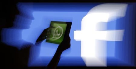 © Reuters. Woman holds a tablet displaying WhatsApp's logo in front of the screen with the Facebook logo in this photo illustration taken in Prague