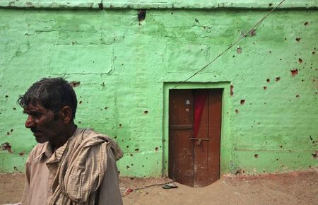 © Reuters. An Indian villager stands next to the wall of a house that locals say was damaged by firing from the Pakistan side of the border at Arnia village
