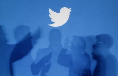 © Reuters. Shadows of people holding mobile phones are cast onto a backdrop projected with the Twitter logo  in Warsaw