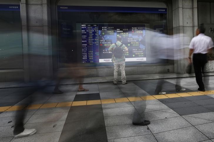 &copy; Reuters A man looks at an electronic board displaying stock prices as passers-by walk past outside a brokerage in Tokyo