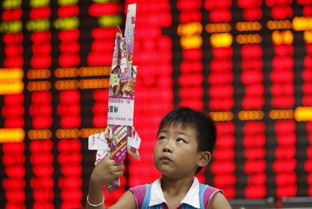 © Reuters. A boy plays with a toy made of paper in front of an electronic screen showing stock information at a brokerage house in Huaibei