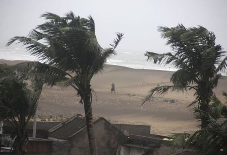 © Reuters. Man walks as strong winds blow along a beach in Gopalpur in Ganjam district