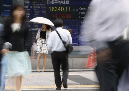 © Reuters. A woman holding a parasol stands as passers-by walk past an electronic board showing Japan's Nikkei average, outside a brokerage in Tokyo