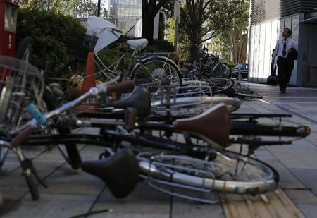 © Reuters. Toppled bicycles lie on a street as a man looks up at the sky while a strong wind caused by tropical storm Vongfong blows in Tokyo