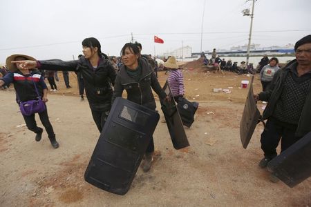 © Reuters. Villagers carry police shields taken from police injured during clashes at Fuyou village in Jinning county, Kunming