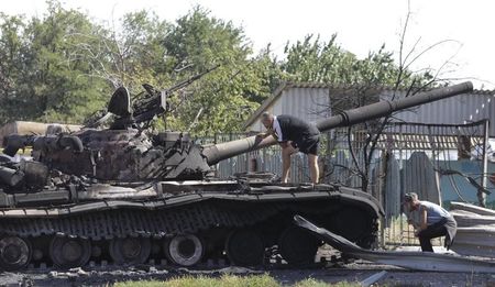 © Reuters. Men inspect a burnt out Ukrainian tank in the village of Kominternovo, on the outskirts of the southern coastal town of Mariupol