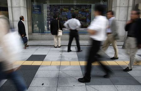 © Reuters. Pedestrians look at an electronic board showing the stock market indices of various countries outside a brokerage in Tokyo