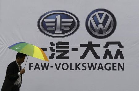 © Reuters. A man holds an umbrella as he walks past a company logo of FAW-Volkswagen at an automobile exhibition in Fuyang