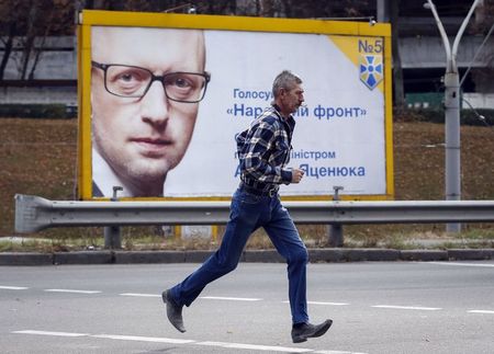 © Reuters. A man runs in front of a pre-election poster with the portrait of Ukrainian Prime Minister Yatseniuk in Kiev